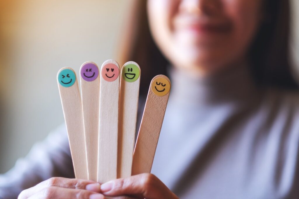 A woman holding colorful hand draw happy emotion faces on wooden stick