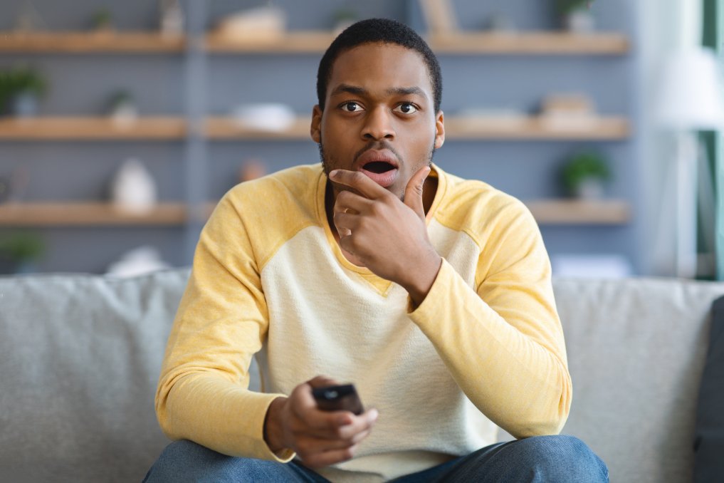 Shocked man with TV remote sitting on couch