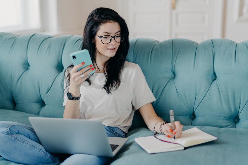 Young Woman Watching Webinar Sofa Phone Laptop Taking Notes