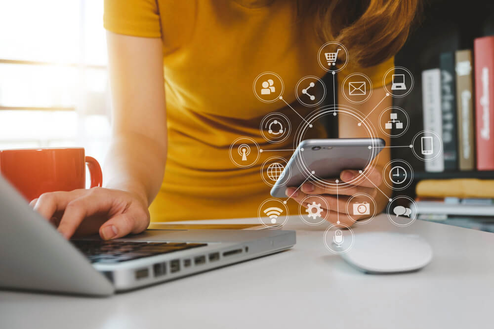 closeup of woman using laptop and phone with hovering social media icons