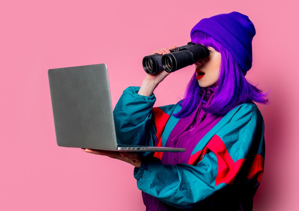 A woman looking at her laptop and conducting keyword research using binoculars