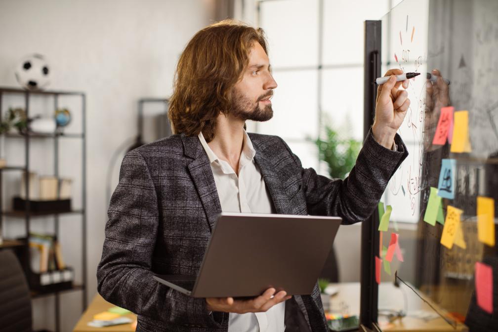 Businessman holding laptop and writing on glass board for his ad testing and experimentation