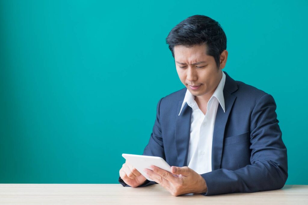 Man sitting at a table looking his tablet, wondering what went wrong with his YouTube backlinking strategy