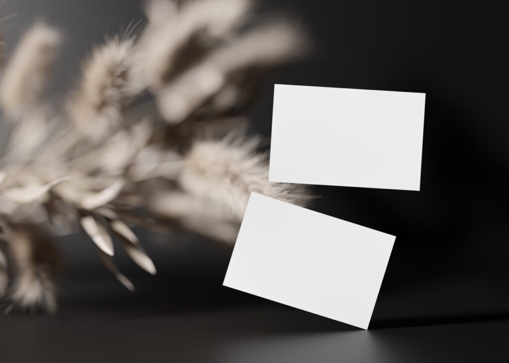 Blank white business cards on black background with dried plants. Mock up for branding identity.
