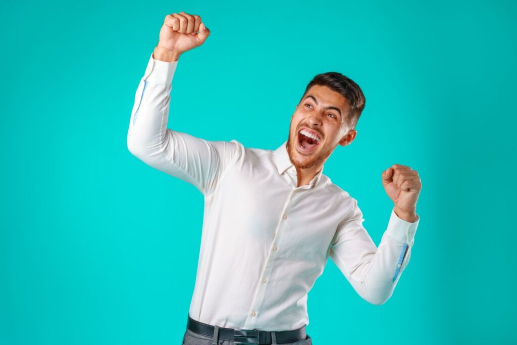Portrait of excited, successful man raising hands up