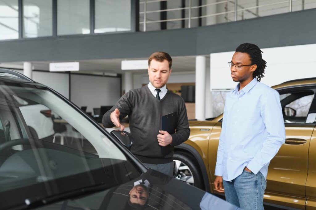 Portrait of male client talking to professional car dealer in dealership.