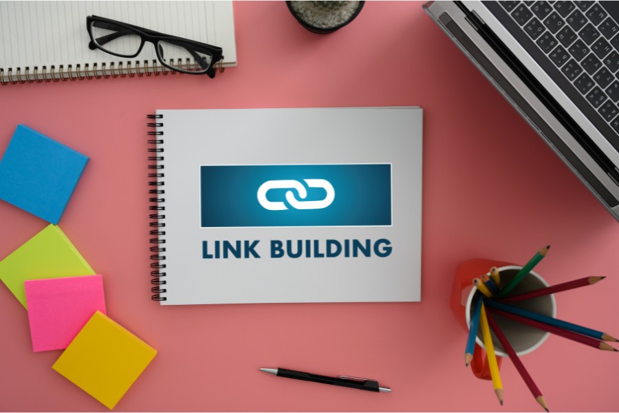 Link building notebook on pink desk with office supplies and laptop